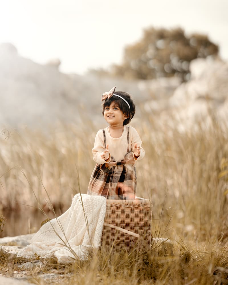 A little girl in a headband standing among tall golden grass outdoors