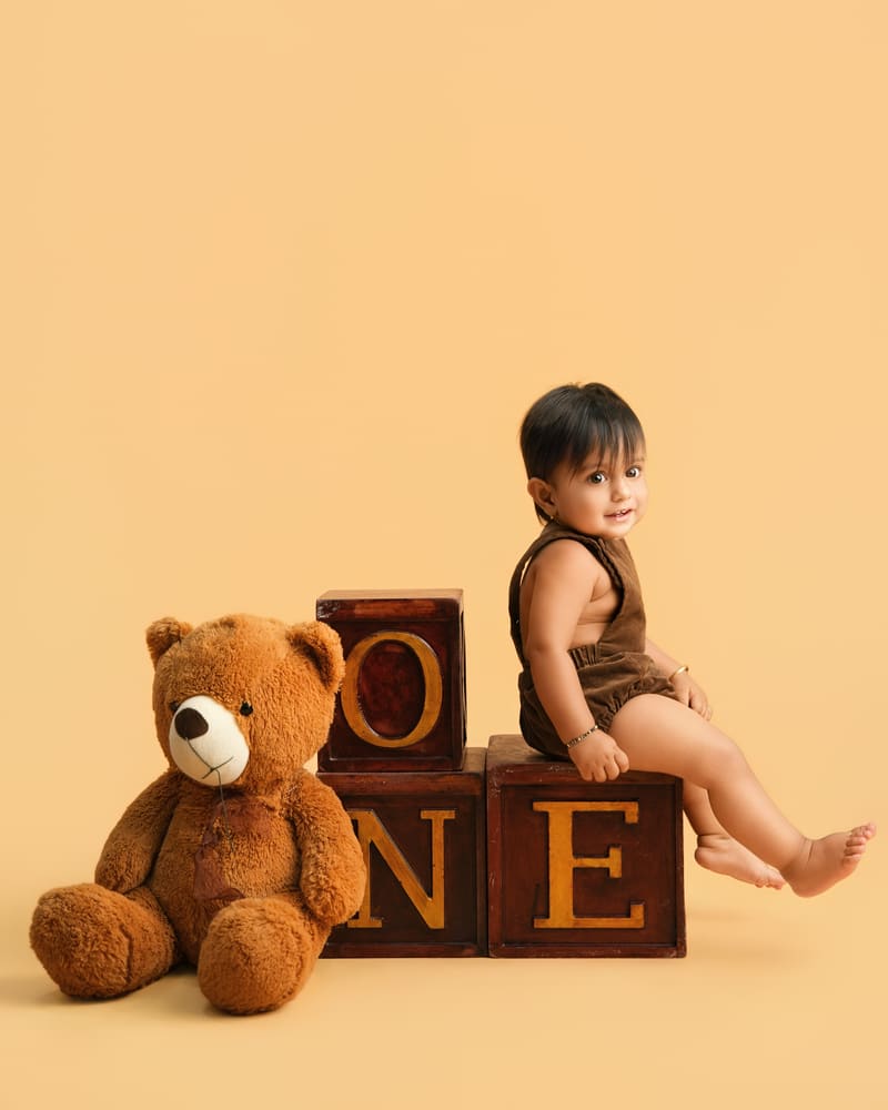 A little boy sitting on wooden ONE blocks beside a big teddy on a peach set