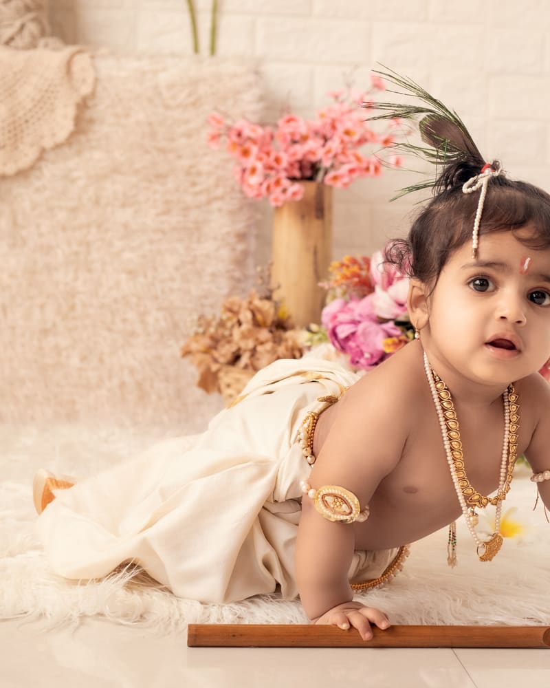 A baby crawling on a cream fur rug, with dried flowers behind