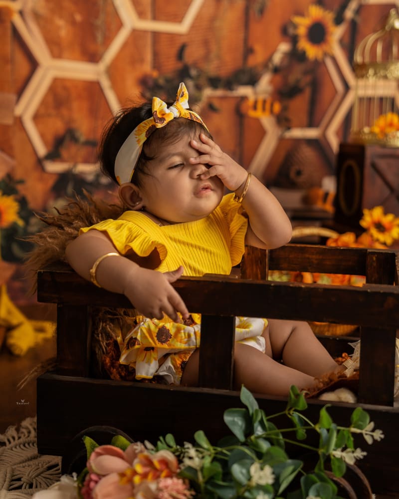 A baby girl in yellow on a honeycomb set with sunflowers