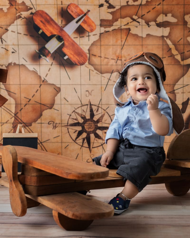 A laughing little boy in an aviator cap on a wooden plane, in front of a vintage map