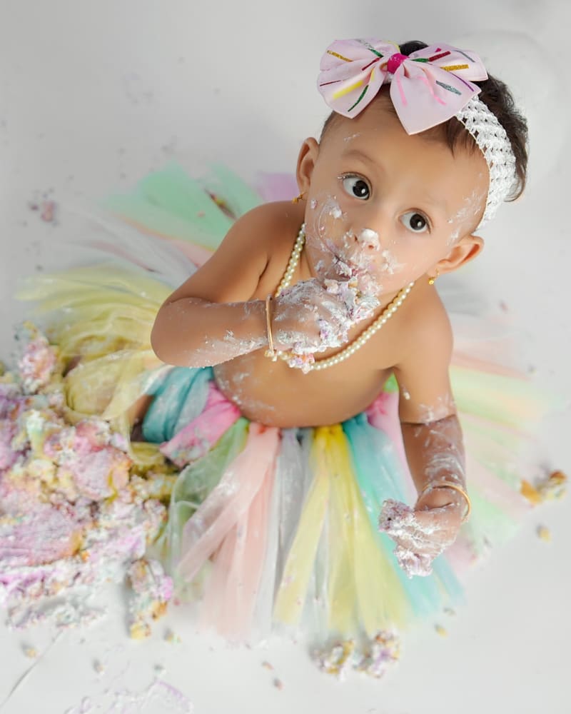 A baby girl in a pastel rainbow tutu during a cake smash